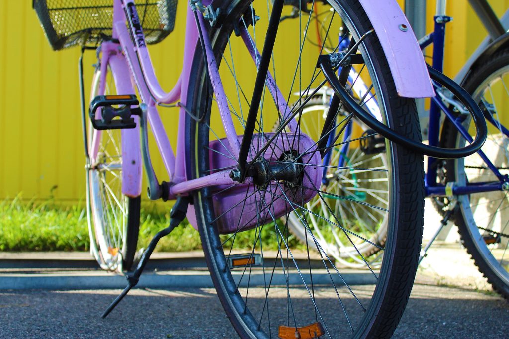 A pink bicycle parked next to a yellow wall in a charming location.
