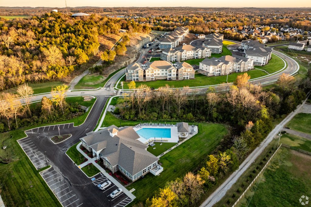 Apartments in Thompson’s Station Aerial view of apartments in Thompson's Station reveals a residential complex with multiple buildings, a central road, parking lots, and a swimming pool embraced by lush trees and greenery. Sanctuary Bluff Apartments in Thompson’s Station