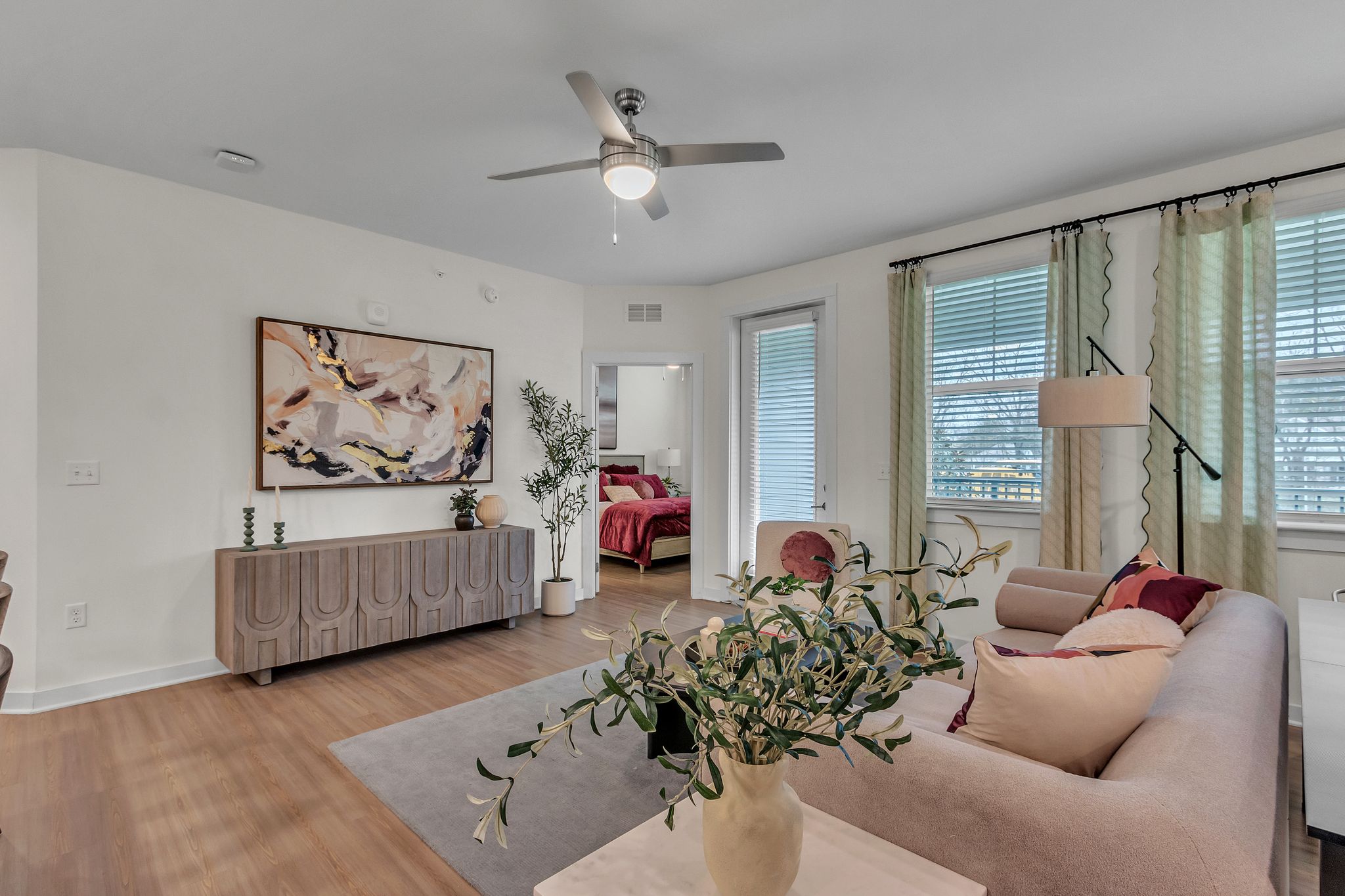 Apartments in Thompson’s Station A contemporary living room with a beige sofa, abstract art on the wall, a wooden sideboard, and a potted plant. A bedroom is visible through a door. Sanctuary Bluff Apartments in Thompson’s Station