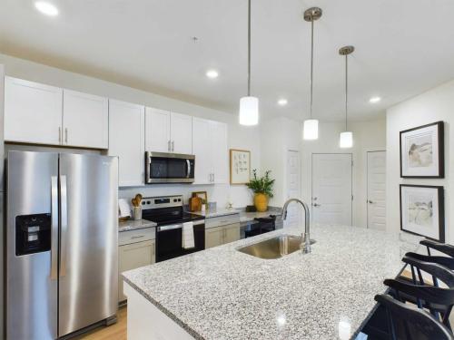 Apartments in Thompson’s Station Modern kitchen with granite island, stainless steel appliances, white cabinets, and pendant lighting. Bar stools are at the island, and framed art is on the wall. Sanctuary Bluff Apartments in Thompson’s Station