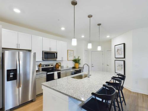 Apartments in Thompson’s Station Modern kitchen with stainless steel appliances, white cabinets, and granite countertops. Features an island with a sink and bar stools, hanging pendant lights, and wooden flooring. Sanctuary Bluff Apartments in Thompson’s Station