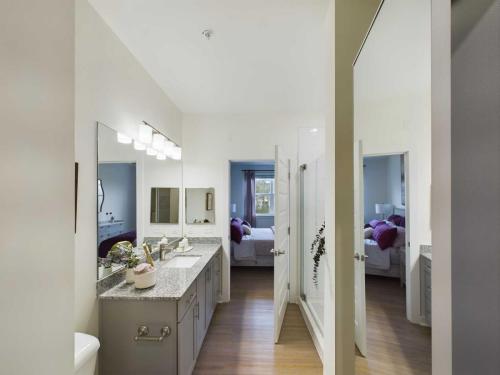 Apartments in Thompson’s Station Modern bathroom with dual sinks, large mirror, granite countertops, and wood flooring. A doorway leads to a bedroom with a bed and window. Sanctuary Bluff Apartments in Thompson’s Station