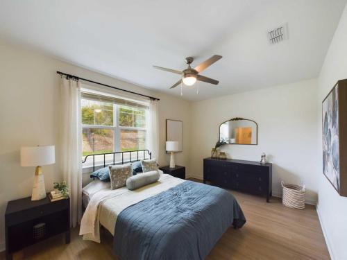 Apartments in Thompson’s Station Bedroom with a neatly made bed, blue bedding, two nightstands with lamps, a dresser with a mirror, a ceiling fan, and a window with curtains. Sanctuary Bluff Apartments in Thompson’s Station