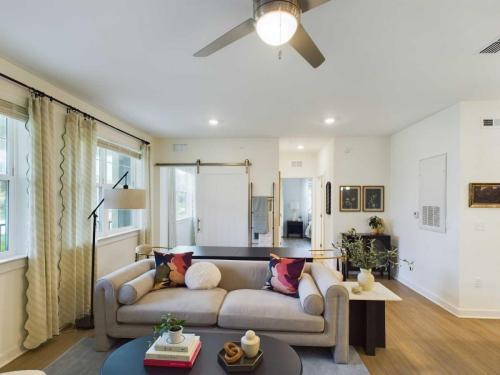 Apartments in Thompson’s Station Living room with a beige sofa, colorful cushions, round black coffee table, overhead fan, potted plants, and large windows with sheer curtains. Sanctuary Bluff Apartments in Thompson’s Station