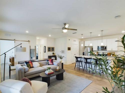 Apartments in Thompson’s Station Open-concept living room and kitchen with modern furnishings, a ceiling fan, and a potted plant. A couch and chairs are arranged around a coffee table, and barstools line the kitchen counter. Sanctuary Bluff Apartments in Thompson’s Station