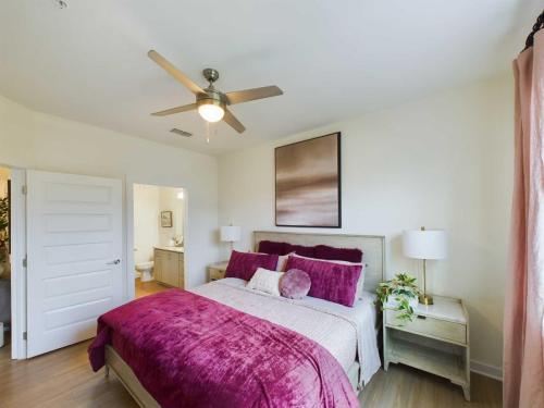 Apartments in Thompson’s Station Bedroom with a bed featuring purple bedding, two bedside tables with lamps, a ceiling fan, and a bathroom visible through an open door. Sanctuary Bluff Apartments in Thompson’s Station