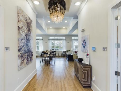 Apartments in Thompson’s Station Spacious lobby with hardwood floors, modern chandelier, large abstract artwork, barstools at a counter, and natural light from large windows. Sanctuary Bluff Apartments in Thompson’s Station