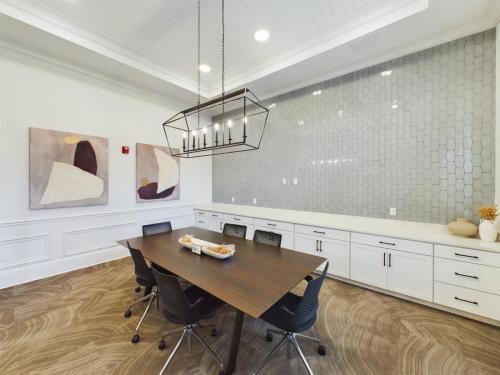 Apartments in Thompson’s Station A modern conference room featuring a long wooden table, black chairs, hanging light fixture, abstract wall art, and white cabinets with a textured gray backsplash. Sanctuary Bluff Apartments in Thompson’s Station