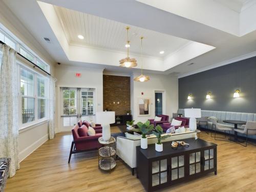 Apartments in Thompson’s Station Contemporary lounge area with sofas, chairs, and coffee tables, featuring ceiling lights and large windows. A small dining area is visible to the right. Sanctuary Bluff Apartments in Thompson’s Station