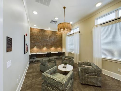 Apartments in Thompson’s Station A modern interior with patterned armchairs around a round table. A brick wall with a long desk and chairs is in the background, and a chandelier hangs from the ceiling. Sanctuary Bluff Apartments in Thompson’s Station