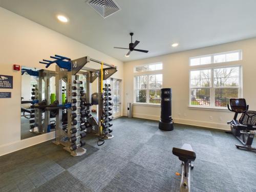 Apartments in Thompson’s Station A gym room with various exercise equipment, including a pull-up station, weights, exercise bikes, and a punching bag, alongside large windows and a ceiling fan. Sanctuary Bluff Apartments in Thompson’s Station