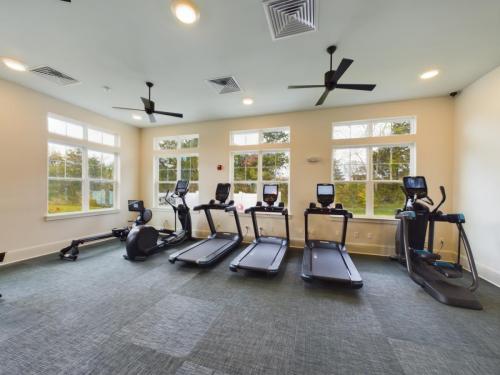 Apartments in Thompson’s Station A well-lit gym room with three treadmills, an elliptical machine, and exercise bike, featuring a row of large windows and ceiling fans. Sanctuary Bluff Apartments in Thompson’s Station