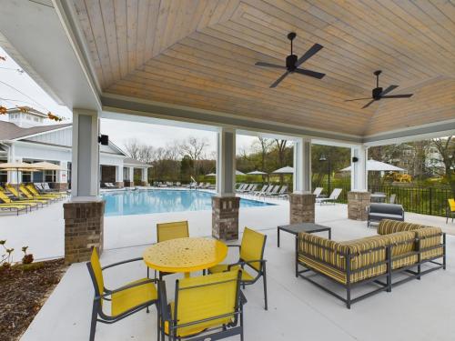 Apartments in Thompson’s Station Outdoor seating area with yellow chairs and striped furniture under a wooden ceiling, facing a swimming pool. Sanctuary Bluff Apartments in Thompson’s Station