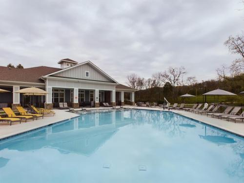 Apartments in Thompson’s Station A large outdoor swimming pool surrounded by lounge chairs and umbrellas, next to a building with a covered patio under a cloudy sky. Sanctuary Bluff Apartments in Thompson’s Station