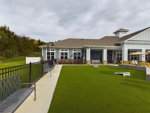 Apartments in Thompson’s Station Outdoor recreational area with green artificial turf, metal benches, a cornhole game, and a modern building with lounge chairs and umbrellas. Overcast sky in the background. Sanctuary Bluff Apartments in Thompson’s Station