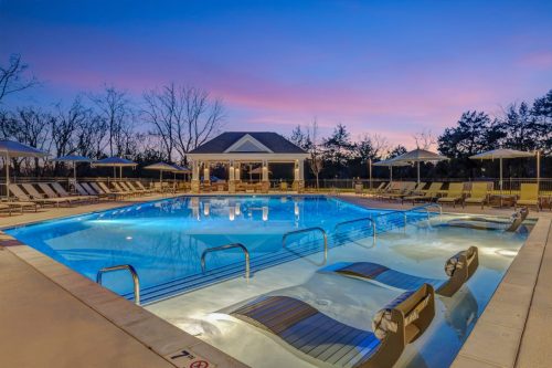 Apartments in Thompson’s Station Outdoor swimming pool with lounge chairs and umbrellas at sunset. A small pavilion is in the background, surrounded by trees with a pink and blue sky overhead. Sanctuary Bluff Apartments in Thompson’s Station