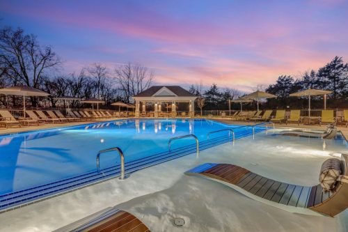 Apartments in Thompson’s Station Outdoor pool area at dusk with loungers and umbrellas around the water. A small pavilion is in the background, surrounded by trees and a colorful sky. Sanctuary Bluff Apartments in Thompson’s Station