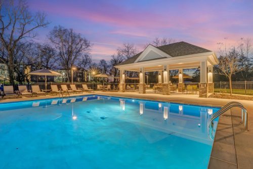 Apartments in Thompson’s Station Outdoor swimming pool area with lounge chairs and a pavilion at dusk, set against a backdrop of trees and a colorful sky. Sanctuary Bluff Apartments in Thompson’s Station